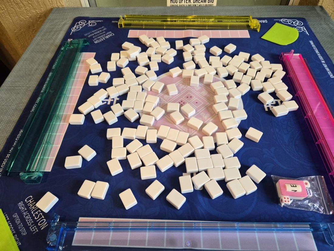Tiles face down on a blue 2F22E mahjong mat, ready to shuffle, with four racks around the edge